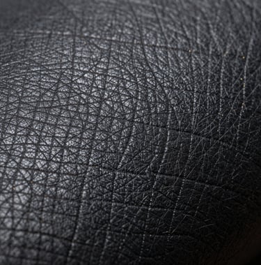 A macro photograph focusing on the rich texture of high-quality dark charcoal leather with subtle metallic gold thread details, symbolizing premium craftsmanship and luxury trade.