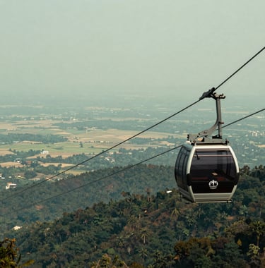 An adventurous photograph from the Phulchoki pick showing a luxury cable car cabin overlooking a vast panorama where the distant flat Terai plains meet the base of the mountains. The colors include pale mist green and deep forest shadows.