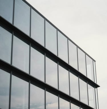 A minimalist architectural detail of a glass and steel building reflecting a cool off-white sky. The composition is geometric and clean, symbolizing structure, clarity, and precision.