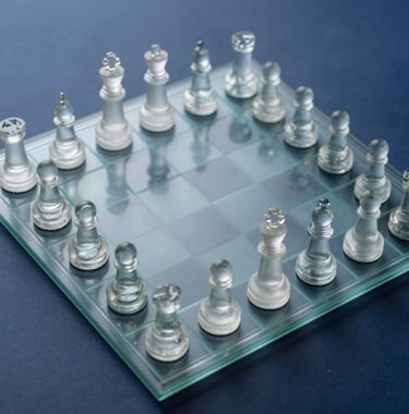 A top-down view of a strategic chessboard with pieces made of glass, reflecting soft mist white light. The background is a deep slate blue surface, suggesting strategic depth and foresight.