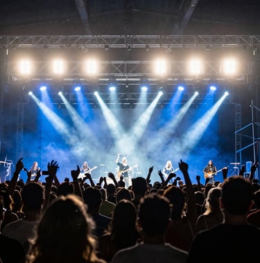 Action shot of a live concert production in Brazil, showing the silhouette of the crowd against bright steel blue and white stage lights, professional photography style.