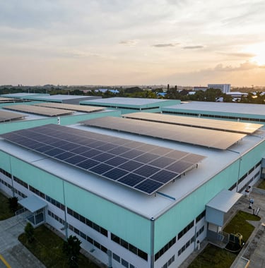 A wide shot of a modern industrial facility in Malaysia during golden hour, with solar panels installed on the roof. The scene is clean and innovative, featuring a palette of dark blue and seafoam.