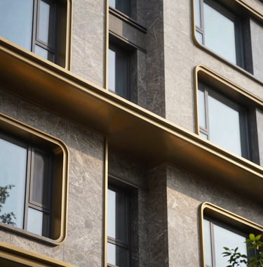 A close-up photograph of architectural detail on a modern upscale residential building in the United States, featuring gold metal accents and dark stone textures under bright daylight.