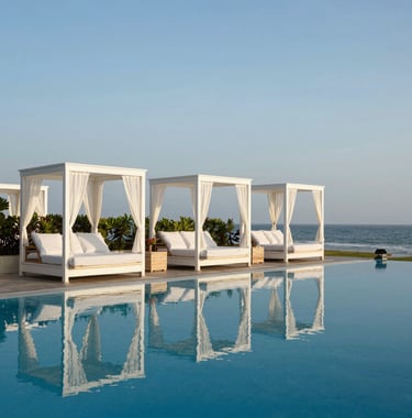 A serene and luxury holiday setting in a South Asian / Indian coastal resort, featuring white cabanas and a deep blue infinity pool reflecting a professional and relaxing travel experience.