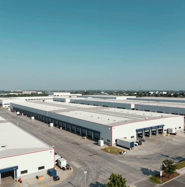Wide shot of a massive logistics hub with modern loading bays. Neat, organized, and showing industrial scale. The sky is a serene teal-blue matching #7BA6A8, projecting operational stability.