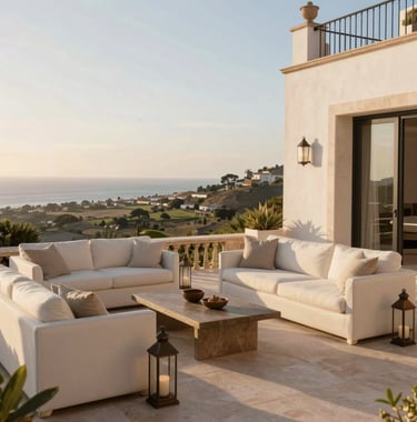 A luxury villa terrace in Portugal at golden hour. The scene features soft off-white outdoor furniture, muted bronze lanterns, and a panoramic view of a coastal valley. High-end lifestyle photography, aspirational and calm.