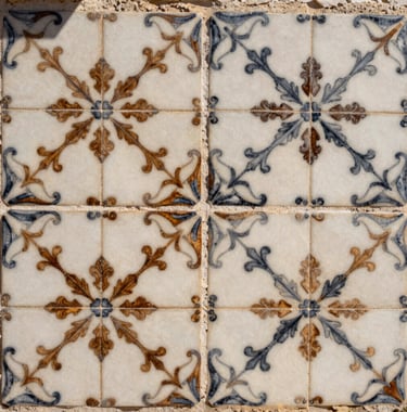 A close-up photography shot of traditional Portuguese hand-painted tiles in soft off-white and charcoal brown patterns, beautifully lit by natural sunlight in a Mediterranean courtyard.