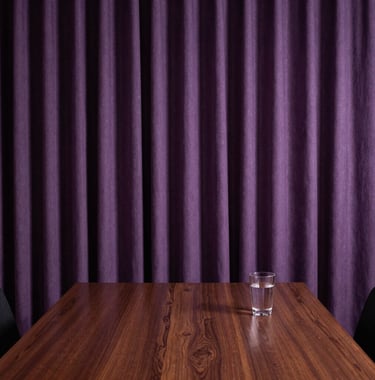 A serene consultation room in Brazil with heavy purple curtains, a dark wooden table, and a small glass of water. Discreet and comforting atmosphere.