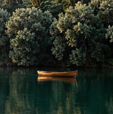 A cinematic shot of a vintage wooden boat gliding silently across a still, emerald-colored lake surrounded by dense, deep olive forests at dawn. Sophisticated and evocative composition.