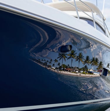Macro photography of a yacht's hull after professional polishing, showing a perfect mirror reflection of the Coastal Florida shoreline and palm trees against a deep navy blue finish.