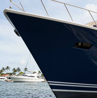A low-angle shot of a freshly painted yacht hull in deep navy blue, showing the sharp, clean lines and the craftsman's attention to detail against the backdrop of a premium Coastal Florida marina.