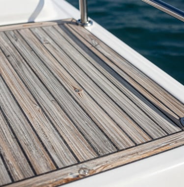 A detailed close-up photograph of a restored teak wood deck on a luxury boat, the rich silver-gray and tan wood grains glowing under the Florida sun, demonstrating precision restoration and high-end detailing.
