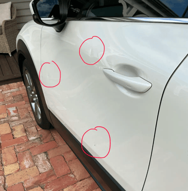 Close-up of small dents and door dings on a white car door circled in red for auto body repair.