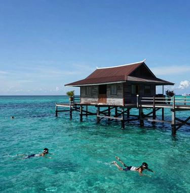 A serene shot of turquoise water and a traditional wooden jetty at Pulau Tidung, Kepulauan Seribu, with clear blue skies and people enjoying snorkeling in a Southeast Asian / Indonesian coastal setting.