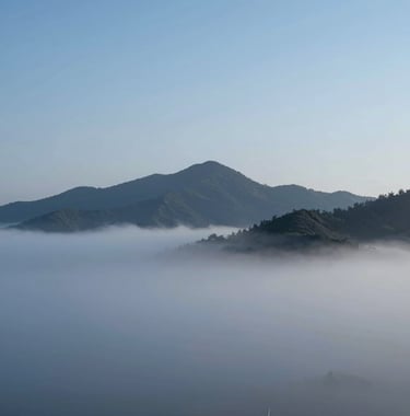 Breathtaking landscape photo of mist-covered mountains at dawn. Minimalist composition with cold blue sky #4A7B8E and sharp charcoal peaks. High-end editorial style.