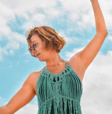 Una muje con vestido de macrame de playa con flecos de macramé verde y gafas de sol bailando 