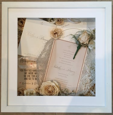 a photo of a memory box full of wedding items and preserved wedding bouquet flowers in a deep frame