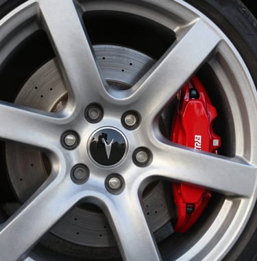 Detailed photography of a premium silver alloy wheel with a red brake caliper, focused on craftsmanship and luxury, outdoor European sunlight.