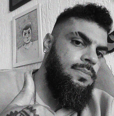 Um homem com barba, e uma tatuagem na mão fazendo joinha