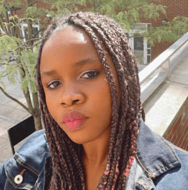 Adachioma Ezeano looks directly at the camera, her hair in braids, she wears a denim jacket.