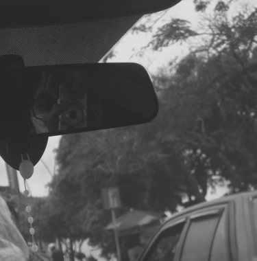 Reflejo de fotógrafo en el retrovisor de un auto entre árboles.