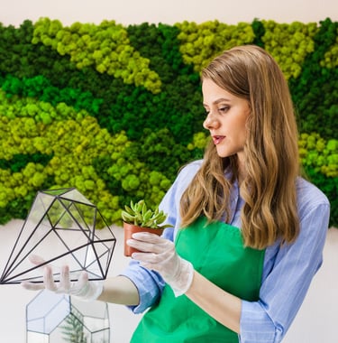 Bir bitki tutan yeşil önlüklü bir kadın. Manisa'da yosun duvar uygulaması ve tasarımı