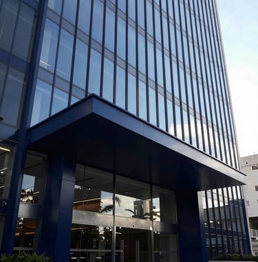 Modern architectural detail of a premium building entrance in a South American / Brazilian capital. High-contrast photography with sharp lines and glass reflections, using a color palette of Deep Navy Blue and Soft Steel Blue to convey reliability and solidez.
