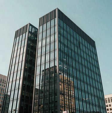 A modern glass-and-steel professional building in a North American business district, captured in clean, bright daylight with teal and charcoal tones.