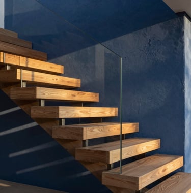 Close-up detail of high-end architectural finishes: a minimalist floating staircase made of oak wood and glass, set against a navy blue textured wall in a modern Spanish mansion. Golden hour sunlight creates elegant shadows.