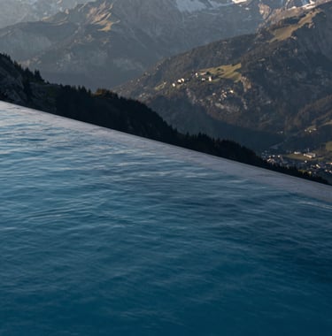 Detail of a luxury infinity pool overlooking the Swiss mountains, sharp architectural edges, deep night blue water, morning sun, high-end photography for an architecture magazine.