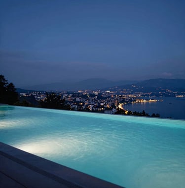 Infinity pool at dusk reflecting a night blue sky, overlooking the Geneva landscape. Clean, quiet luxury aesthetic, high-end real estate magazine style.