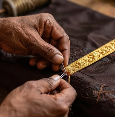 Macro photography of a skilled artisan's hand in South Asian attire, using a needle to weave gold zari thread on dark silk. Warm lighting.