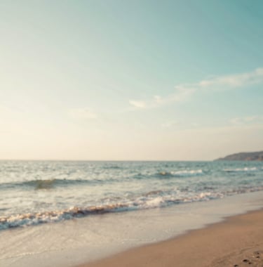 A tranquil photo of a hidden beach at sunset, with soft waves lapping the shore. The sky is a mix of #A8C9CF and warm off-white tones, evoking a sense of peaceful wanderlust and discovery.