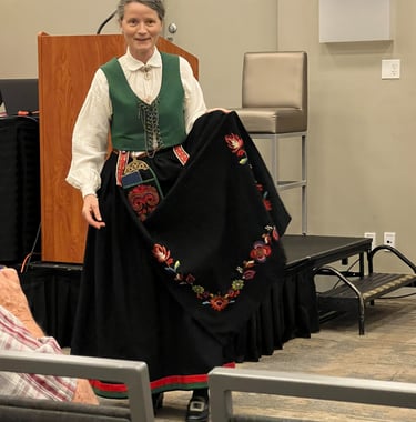 A woman in a bunad with a green vest holding the apron to show detail