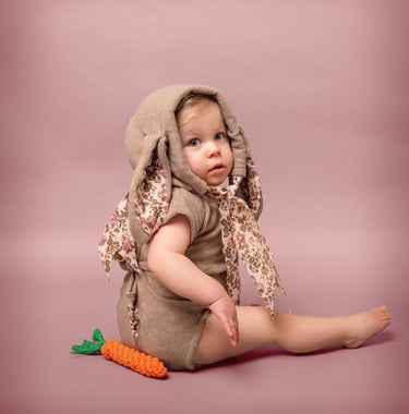 a baby in a bunny suit with a carrot on the ground