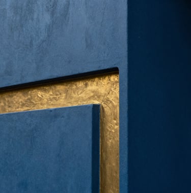 Architectural detail of a luxury Indian estate in Lonavala. A smooth, deep blue concrete wall meets a warm gold metallic inlay. The lighting is soft and indirect, creating a sense of depth and premium texture. 8k close-up photography.