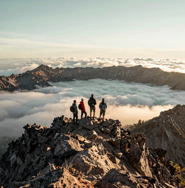 A stunning wide photograph of Global Adventure Travelers standing on the rocky summit ridge of Mount Rinjani at sunrise, looking out over a sea of clouds. Rugged volcanic terrain, sharp details, pristine morning light, off-white and pale sage green tones in the sky.
