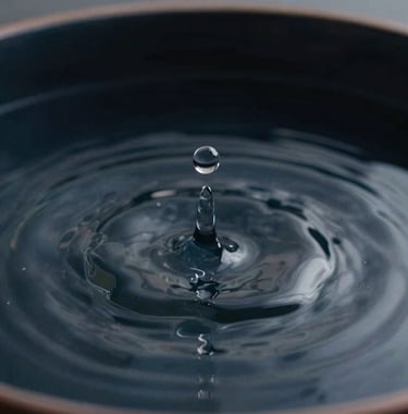 A macro shot of a single drop of water falling into a still basin of dark navy water. The ripples are perfectly symmetrical and clean. The aesthetic is premium, soulful, and evocative of a meditative pause.