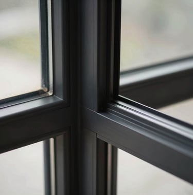 A sharp, detailed close-up shot of an ultra-thin matte black window profile. The focus is on the precision-engineered corner joint and the sleek, minimal frame. High-end architectural product photography style.