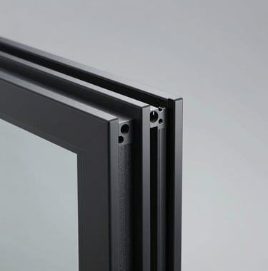 A detailed close-up of a sleek, ultra-thin matte black aluminum window profile meeting a clear glass edge. The composition highlights the precision engineering and industrial-luxury finish against a soft grey background.
