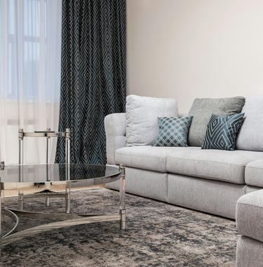 Gray sectional sofa styled with layered throw pillows in blue and gray patterns, patterned curtains,