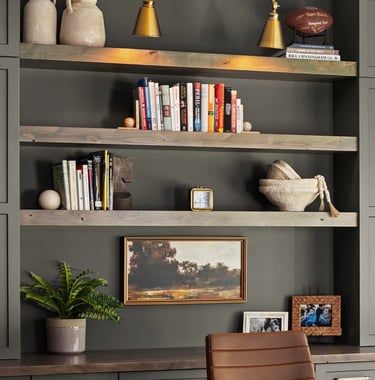 Dark gray shelving unit styled with books, ceramic vessels, brass pendant lights, framed artwork, an