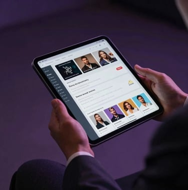 A professional close-up of a person in an expensive suit holding a digital tablet. The tablet shows data visualizations and influencer profiles. Soft, premium lighting with dark purple shadows. North American / US.