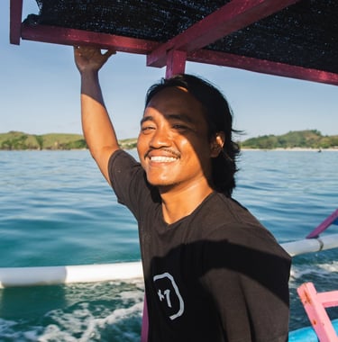 Our surf instructor smiling on a traditional boat on the blue ocean water in Lombok, Indonesia.