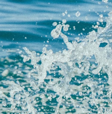 A close-up of dynamic ocean water splashing with white foam and droplets against deep blue waves.