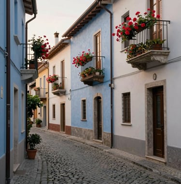 A narrow cobblestone street in an Italian village, colorful walls in muted blue and off-white, vibrant flowers on balconies, soft afternoon sunlight.
