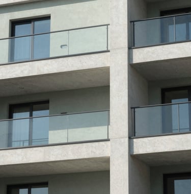 A detailed shot of modern architectural details on a residential building, showing clean concrete lines and glass, with a Soft Sage accent wall in the background under clear International daylight.