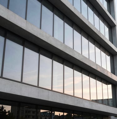 A wide photography shot of a sleek, modern architectural building detail featuring clean lines and large glass panels reflecting a soft sunset. The style is contemporary and reflects international design standards.