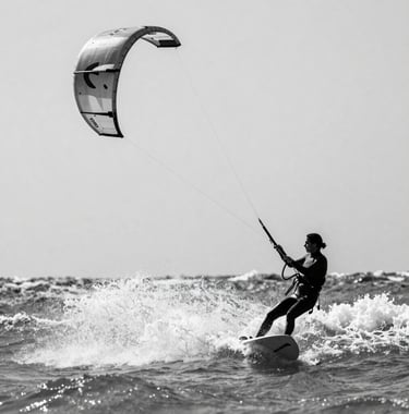 A candid, sharp photo of Ligia kite-surfing, her silhouette dark against the white spray of a wave. Energetic yet curated, #2C3539 and #FAF8F5.