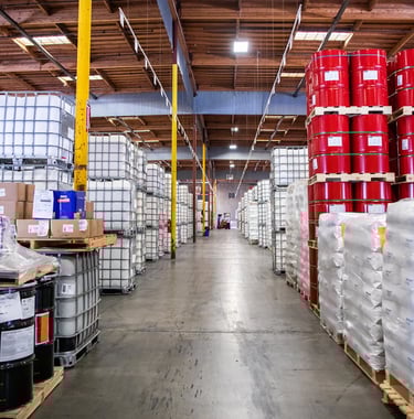 Warehouse with barrels stacked on pallets containing chemicals, acids, solvents, and caustic lye